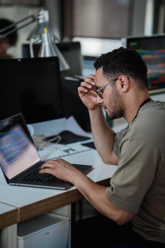 A man intensely focused on coding at a desk in a modern office environment.